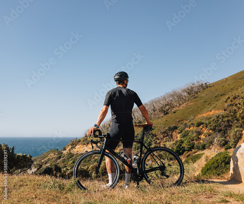 Back view of a male cyclist leaning on his road bike relaxing during training, enjoying the view