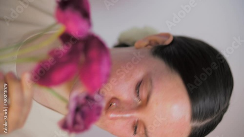 Female model posing with flowers. Close-up portrait 4K video. The young and attractive dark hair actor with dark eyes. Skincare concept video for social media. 