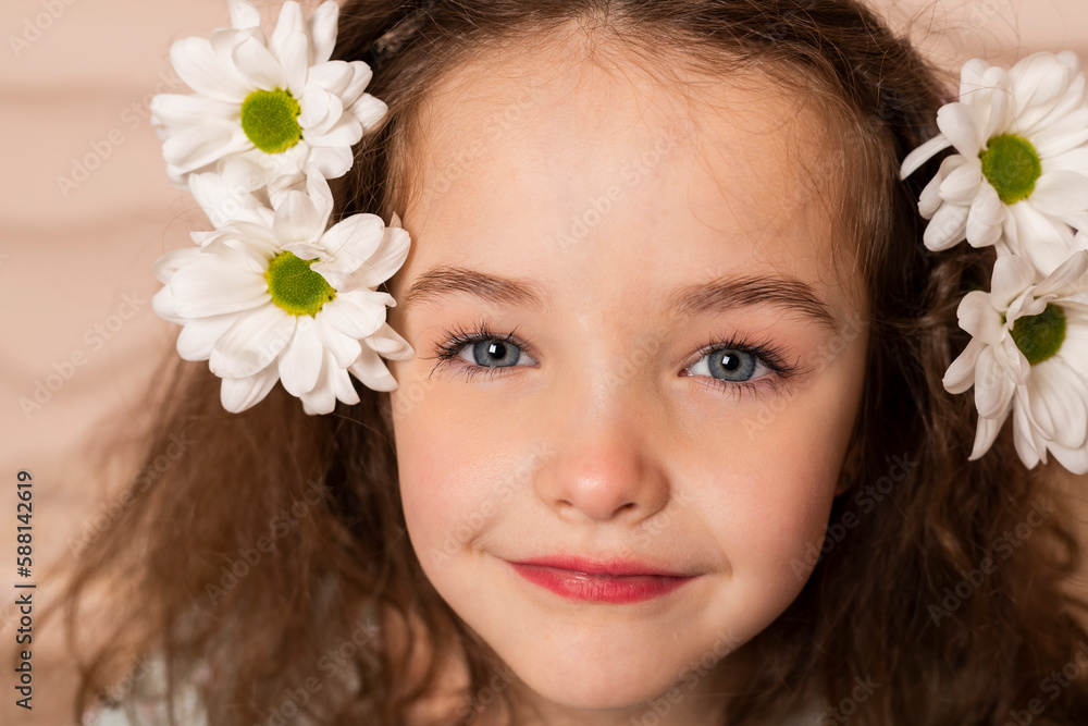 Close-up Portrait of a charming little girl, well dressed in a pastel green dress with a slight makeup and brown loose hair, posing with a chamomile flowers over a beige wavy background. Close-up Portrait of a charming little girl, well dressed in a pastel green dress with a slight makeup and brown loose hair, posing with a chamomile flowers over a beige wavy background.