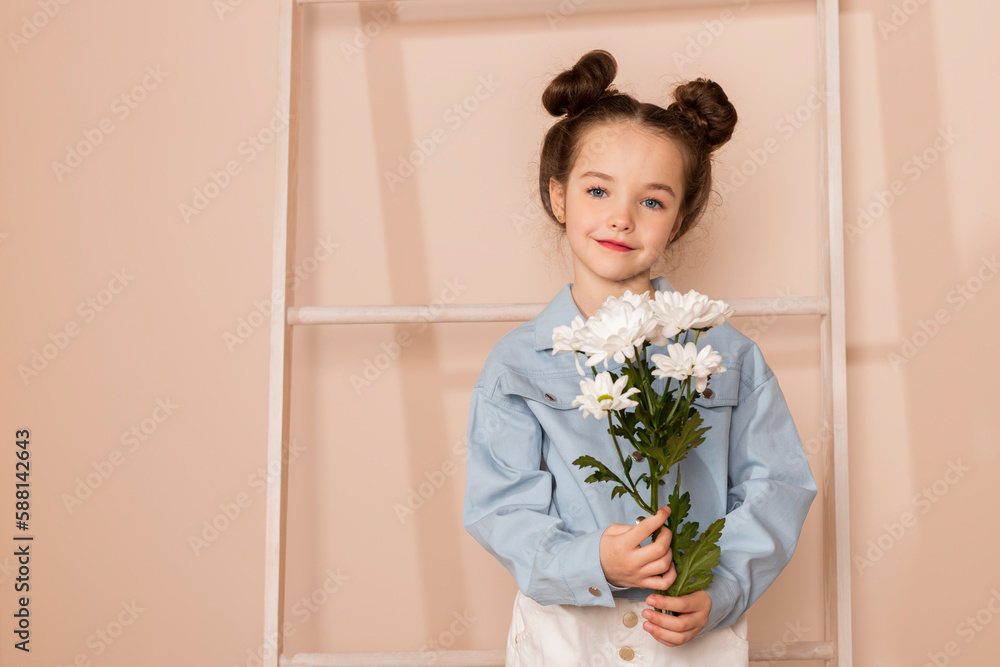 Portrait of a charming little girl, well dressed in a blue shirt and white pants or trousers and with a slight makeup and double bun hair. Isolated on pastel beige background. Portrait of a charming little girl, well dressed in a blue shirt and white pants or trousers and with a slight makeup and double bun hair. Isolated on pastel beige background.