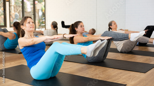 Positive fit young woman doing v-sit to strengthen abs muscles during warming up before group training in pilates studio