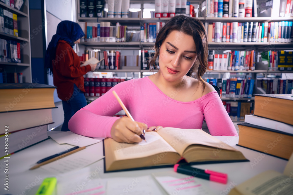 Young, beautiful student girl who studies at the library and writes notes. The girl is studying and preparing for the exam. Young, beautiful student girl who studies at the library and writes notes. The girl is studying and preparing for the exam.