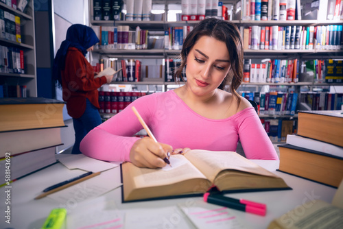 Young, beautiful student girl who studies at the library and writes notes. The girl is studying and preparing for the exam.