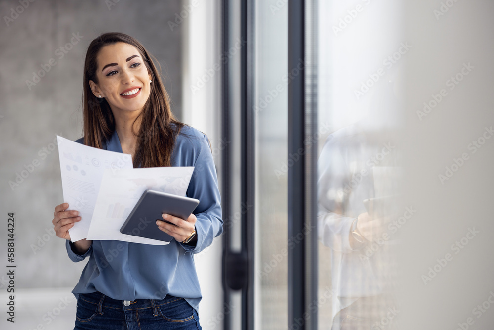Smiling businesswoman standing in modern office with digital tablet Smiling businesswoman standing in modern office with digital tablet