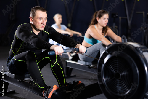 Athlete is engaged in the gym, man works on the rowing simulator