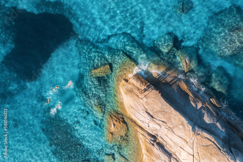 Aerial view of swimming people in blue sea, rocky beach, waves at sunset in summer in Sardinia, Italy. Tropical background. Landscape. Transparent azure water and stones. Top drone view. Down view © den-belitsky