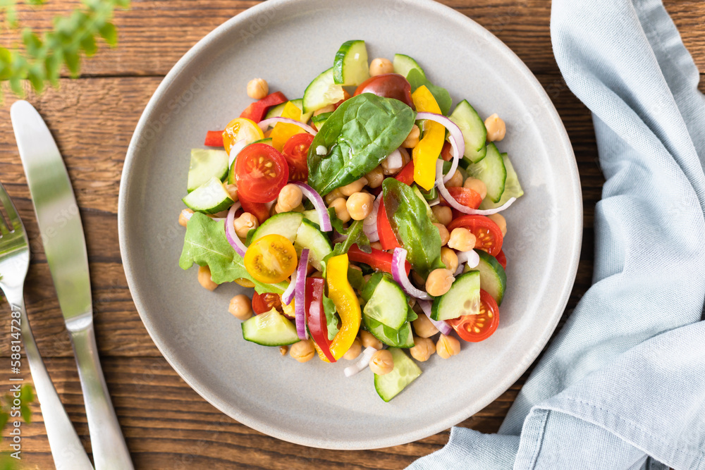 Vegetarian vegetable salad with chickpeas, tomatoes, red onions, cucumbers and lettuce. Vegetarian food rich in protein and fiber. Vegetable salad on wooden table top view Vegetarian vegetable salad with chickpeas, tomatoes, red onions, cucumbers and lettuce. Vegetarian food rich in protein and fiber. Vegetable salad on wooden table top view