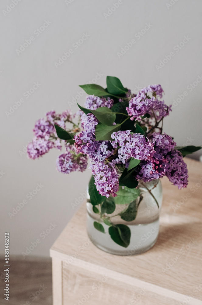 Bouquet of garden lilacs in a glass vase on a wooden bedside table. Bouquet of garden lilacs in a glass vase on a wooden bedside table.