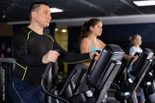 Fit male athlete working out at elliptical machine in gym