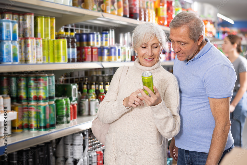 Elderly couple choosing carbonated drinks together in aluminum cans in the grocery section of a supermarket