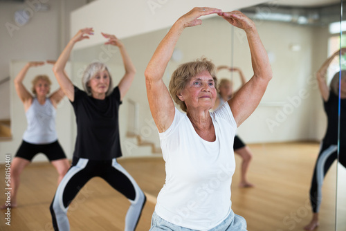 Mature women who are engaged in the dance section in the studio at a group lesson perform a plie squat, being in the position ..of a ballet stand