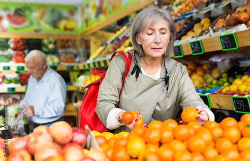 Woman selecting tangerines in greengrocer. Man walking in background