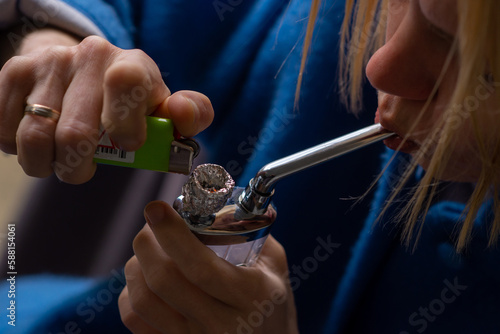 A woman lights a marijuana bong. Cannabis smoking device. A means of relaxation, concentration.