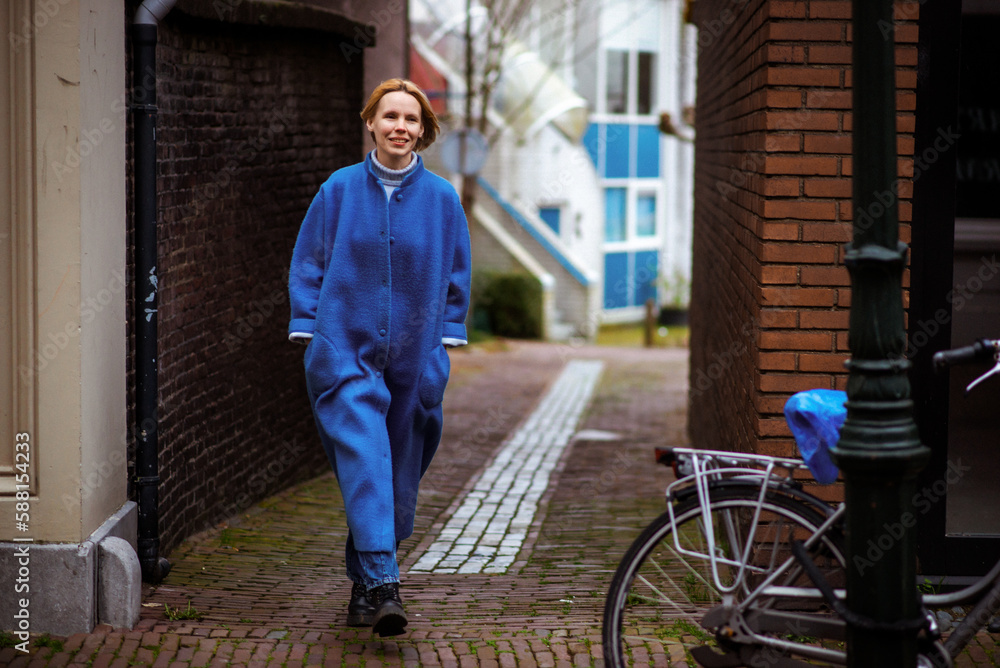 Weekend in the Netherlands, a woman in a blue coat walks along the road. Rest, travel in Europe.