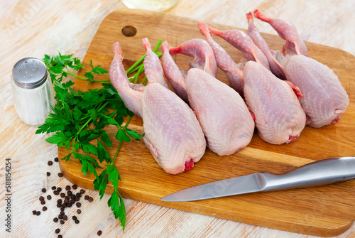 Uncooked quails on wooden board with parsley, black pepper and knife.