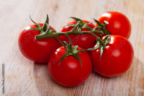 Closeup of fresh ripe tomatoes on branch on wooden surface. Organic vegetables concept