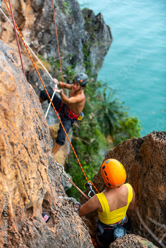 Asian family mother and son helping each other during climbing on rocky mountain together at tropical island. Man and woman enjoy outdoor active lifestyle and extreme sport climbing on summer vacation