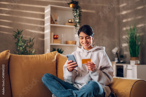 Quadro su tela Woman using smartphone and holding credit card while online shopping from home