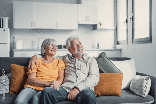 Dreamy middle aged senior loving retired family couple looking in distance, planning common future or recollecting memories, enjoying peaceful moment relaxing together on cozy sofa in living room.