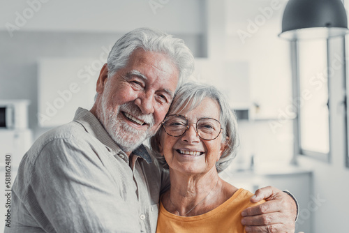 Headshot portrait of smiling elderly 60s husband and wife standing relax hugging cuddling, happy mature old couple rest in living room embrace look at camera show love and care.