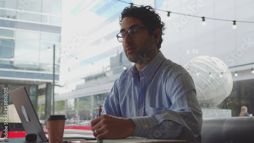 Middle-aged Latin businessman interviewing for a job in a coffee shop and taking notes in a notebook. Copy space.