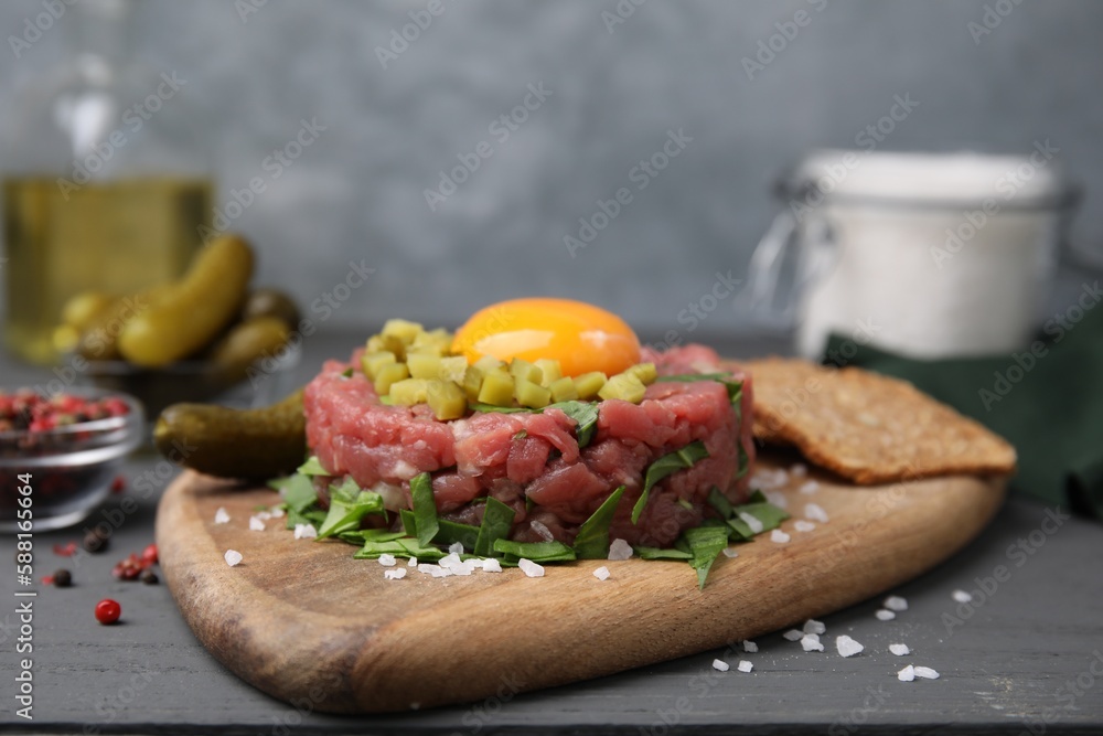 Tasty beef steak tartare served with yolk, pickled cucumber and other accompaniments on grey wooden table