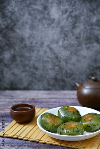 A plate of Qingtuan stuffed with egg yolk and dried meat floss, a cup tea and a teapot on wooden table. Traditional seasonal Chinese delicacies in Jiangnan area around the time of Tomb Sweeping Day. 
 photo