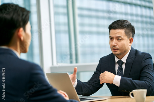 Canvas Print two asian corporate executives sitting at desk discussing business in office
