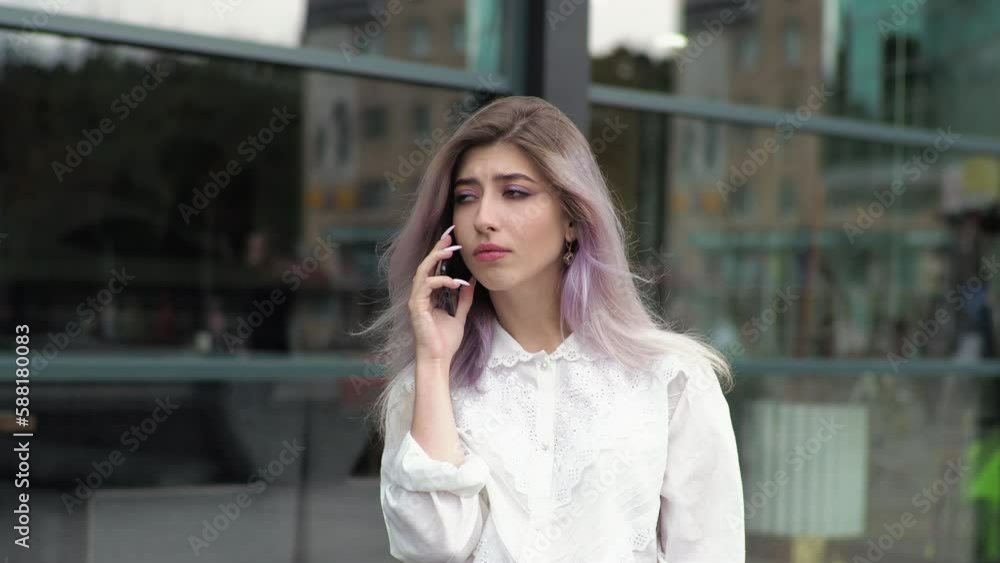 A young business woman stands against the background of a window outside, talking on a mobile phone. A young business woman stands against the background of a window outside, talking on a mobile phone.