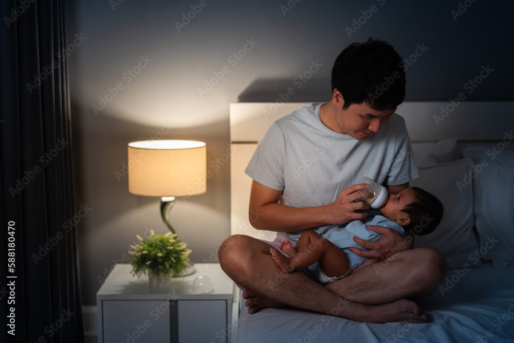father feeding milk bottle to her newborn baby on bed at night father feeding milk bottle to her newborn baby on bed at night