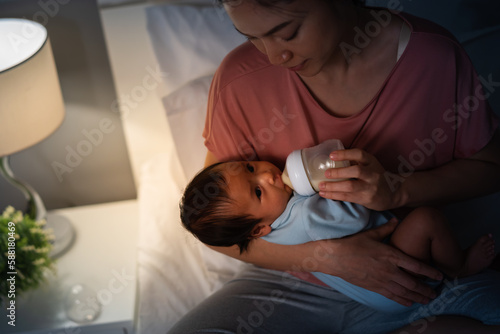 mother feeding milk bottle to her newborn baby on bed at night