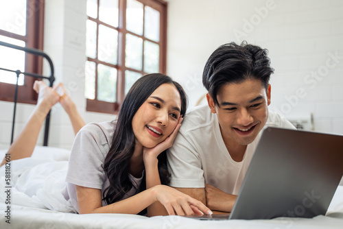 Asian attractive woman using laptop on bed with husband in the morning. 
