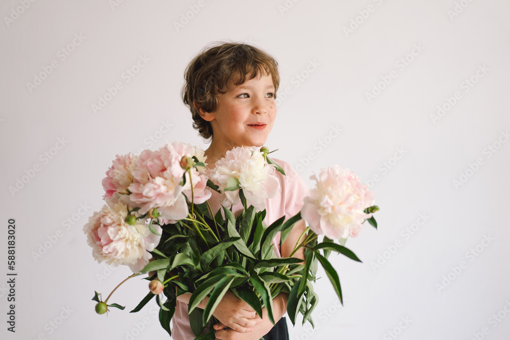 Cheerful happy child with Peonys bouquet. Smiling little boy on white background. Mother's Day. Love and romantic concept