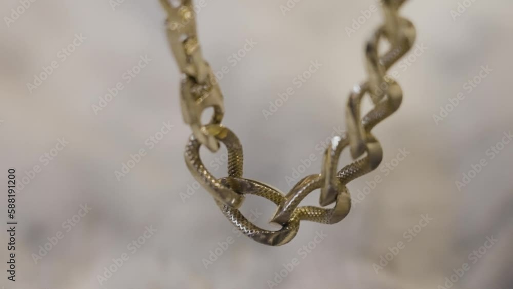 A gold link chain gently hanging into frame and moving slowing in slow motion. A gold link chain gently hanging into frame and moving slowing in slow motion.