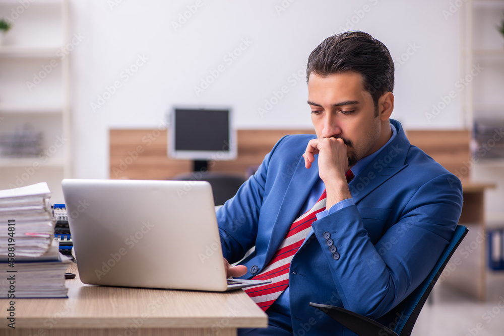Young male employee unhappy with excessive work at workplace Young male employee unhappy with excessive work at workplace