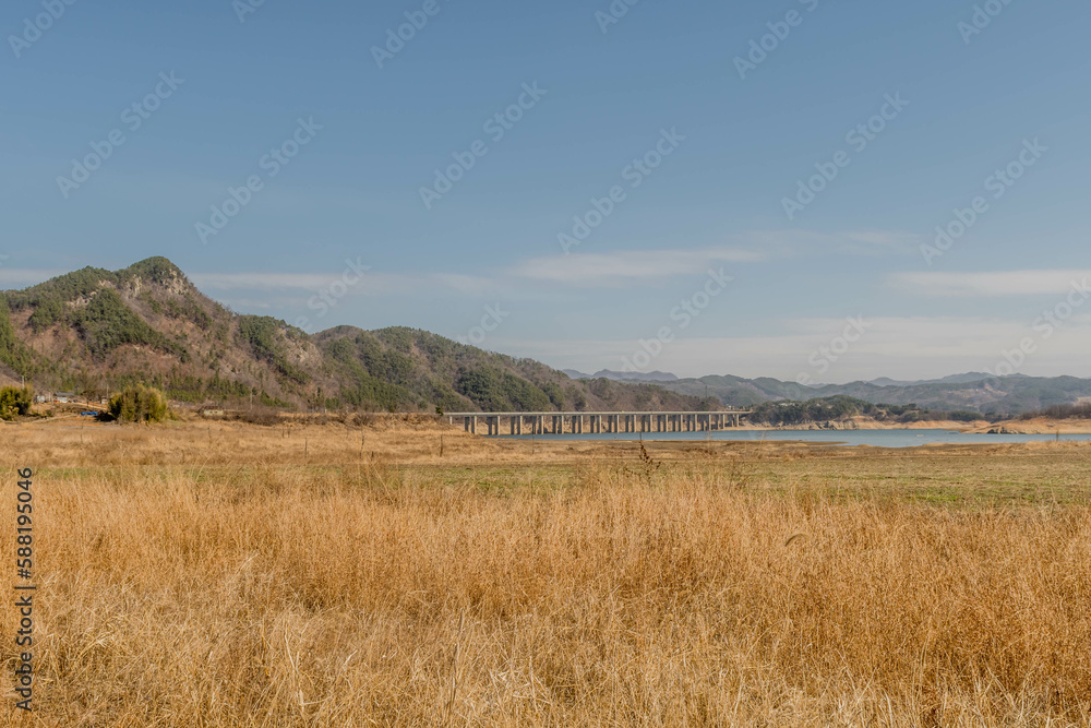 Landscape of field in rural area with lake and bridge in distance..