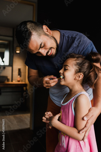 latin young father teaching to his daughter how to brush teeth at home in Mexico Latin America