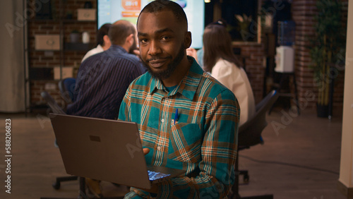 African american office employee working on laptop portrait, front view. Smiling man holding computer, looking at camera medium shot, company financial presentation, business meeting