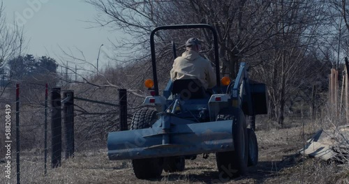 Slow motion back on shot of a man driving a blue tractor along uneven terrain photo