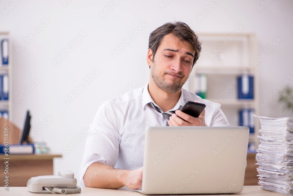 Young male employee unhappy with excessive work in the office Young male employee unhappy with excessive work in the office