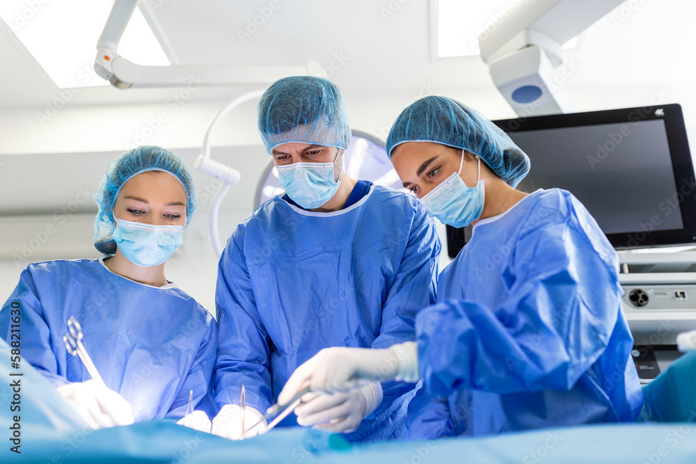 Group of medical team urgently doing surgical operation and helping patient in theater at hospital. Medical team performing surgical operation in a bright modern operating room Group of medical team urgently doing surgical operation and helping patient in theater at hospital. Medical team performing surgical operation in a bright modern operating room
