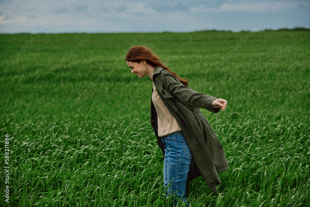 red-haired, happy woman stands in a green field in rainy weather. Emotions, harmony with nature