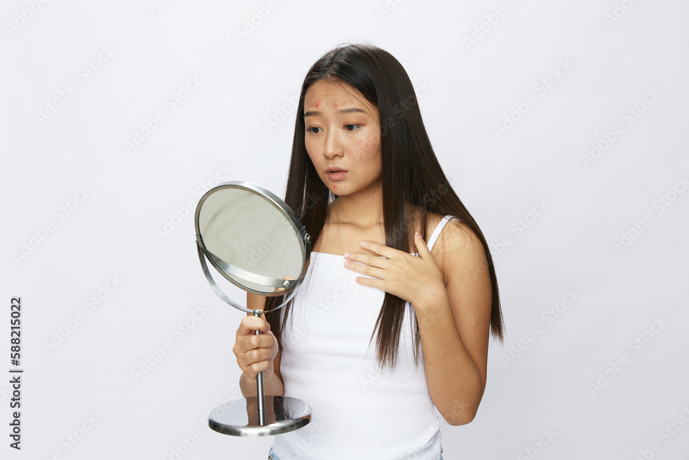 Asian woman with mirror in hand facial skin problems, acne and inflammation, red rash and allergies, chicken pox, sadness from rashes. Facial skin care concept for diseases and nerves Asian woman with mirror in hand facial skin problems, acne and inflammation, red rash and allergies, chicken pox, sadness from rashes. Facial skin care concept for diseases and nerves