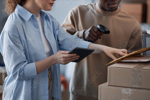 Young female manager of post office or storage room with tablet pointing at envelope with letter while checking number of packet or address