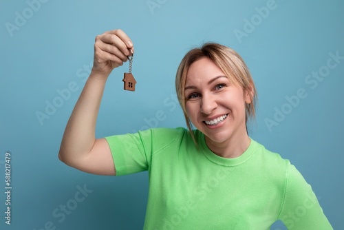 horizontal photo of a young mother in a casual outfit who holds a keychain from the keys of the apartment on a blue background
