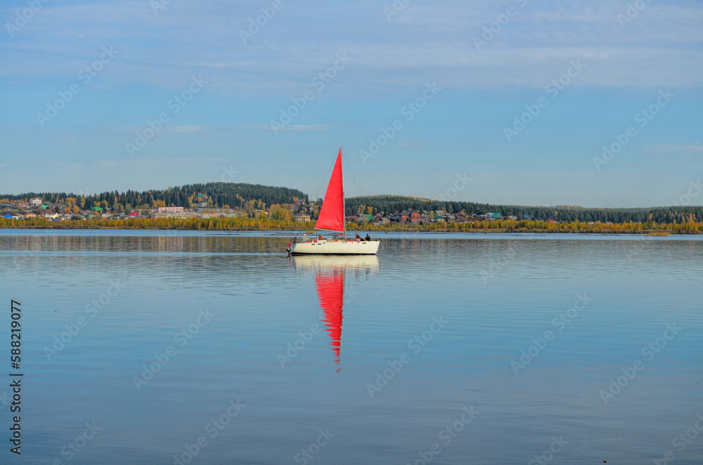 Fototapeta premium a white yacht with a red sail floats on the mirror surface of the lake