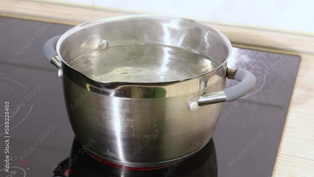 Stationary video of transparent boiling water in stainless steel pot without lid, with steam vapor on black inductive stove panel. Soup preparation, easy cooking at home. Modern kitchenware tools Stationary video of transparent boiling water in stainless steel pot without lid, with steam vapor on black inductive stove panel. Soup preparation, easy cooking at home. Modern kitchenware tools