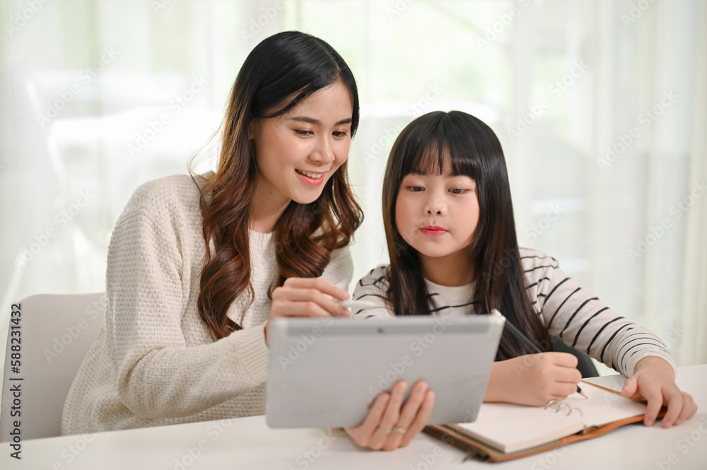 Caring Asian female sister teaching online lesson to her little sister