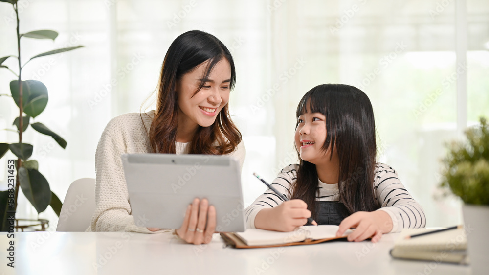 Friendly Asian female sister teaching math to her little sister, looking at tablet screen together Friendly Asian female sister teaching math to her little sister, looking at tablet screen together