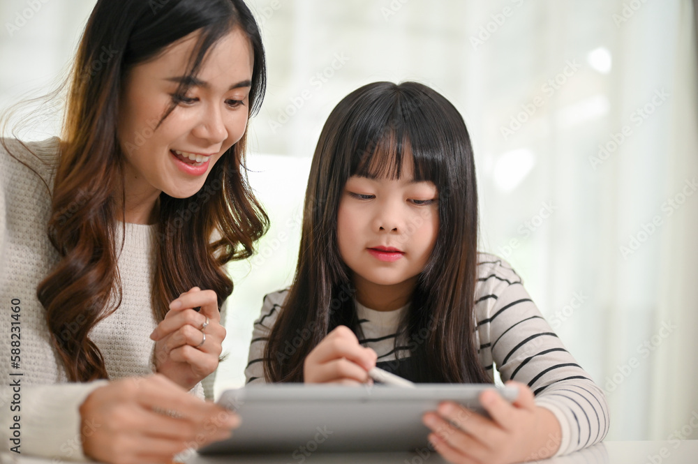 Attractive Asian mom or tutor teaching math on a tablet to a little girl at home. Attractive Asian mom or tutor teaching math on a tablet to a little girl at home.